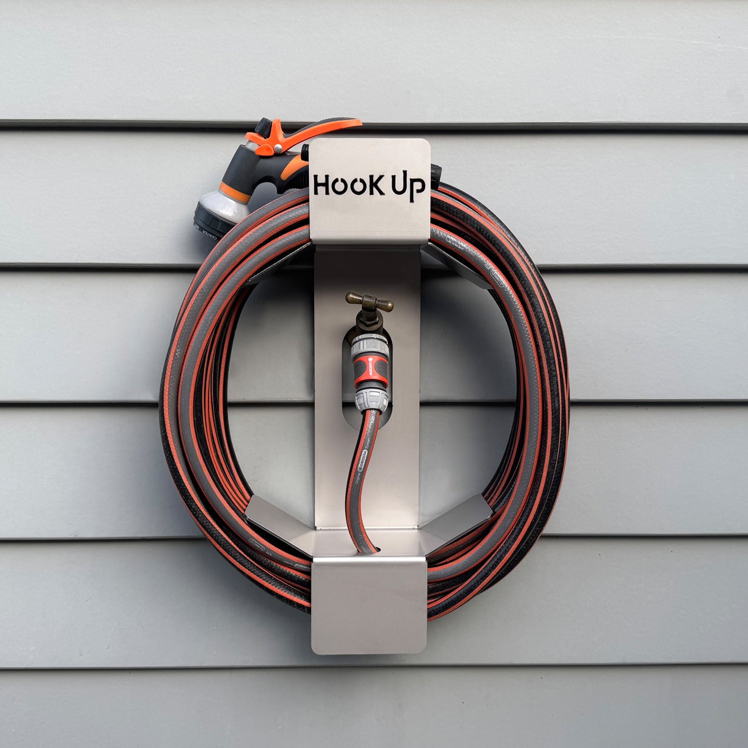 Coiled garden hose with nozzle on a 'Hook Up'Original reel mounted on hose faucet/tap